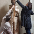 Sala di un museo: due studenti misurano l'altezza di una scultura lignea che ritrae un vescovo